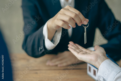 Real estate agents and sales representatives hand out keys from new homes to office clients with examples of homes laid out in front.