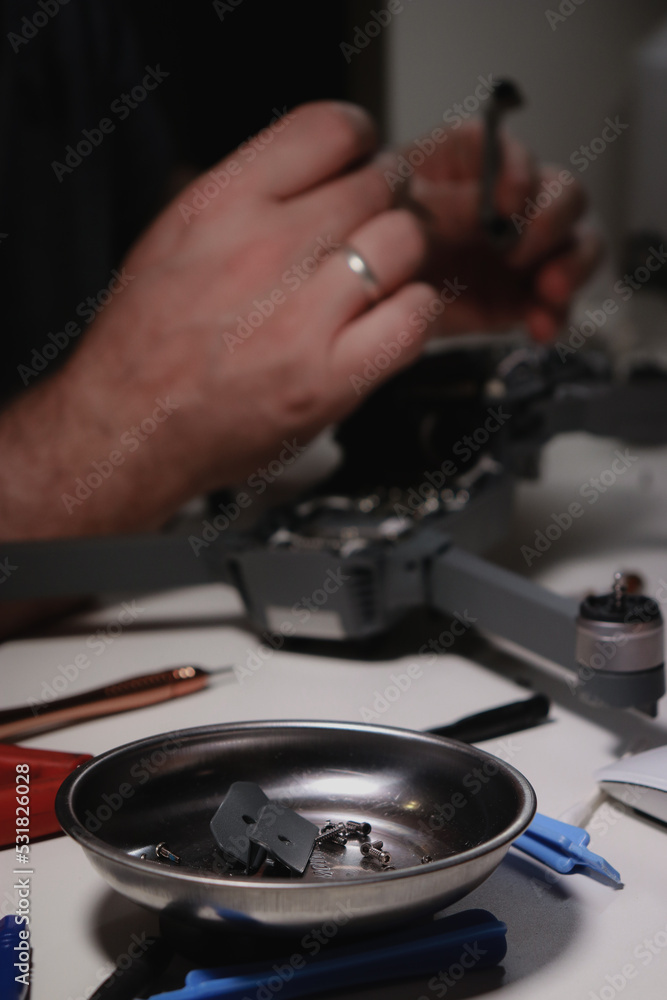 close up of mans hands repairing a drone on white table with different tools