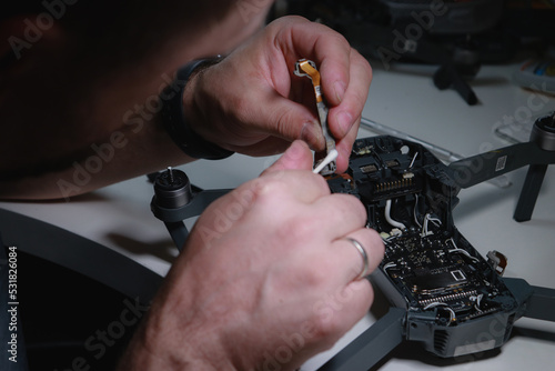 close up of mans hands repairing a drone on white table with different tools