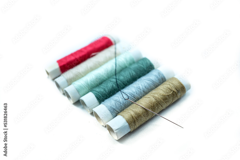 Rows of sewing threads of various colors and sewing needles isolated on white Rows of sewing threads of various colors and sewing needles isolated on white