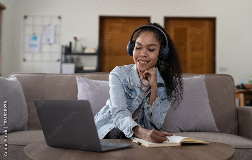 mixed race woman wearing headphones watching webinar write notes study online with online teacher, african female student learning language computer course on laptop listen translate lecture mixed race woman wearing headphones watching webinar write notes study online with online teacher, african female student learning language computer course on laptop listen translate lecture