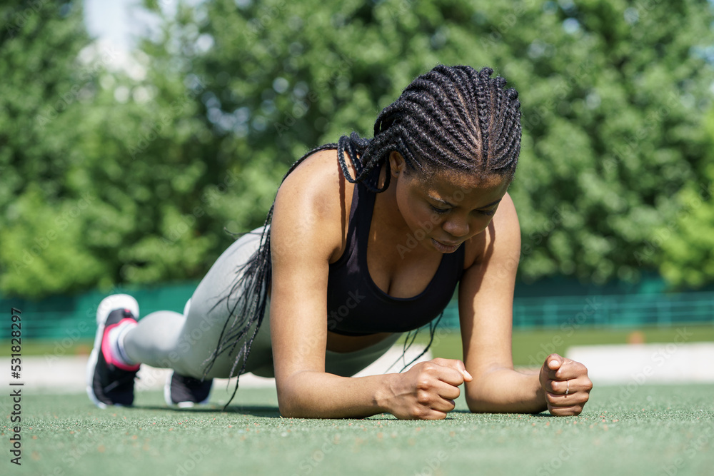 Φωτογραφία Young female person in sportswear does plank exercise to strengthen body on green turf flooring