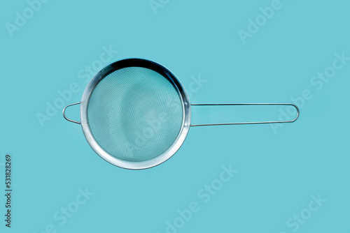 Stainless steel strainer for filtering tea with water isolated on turquoise