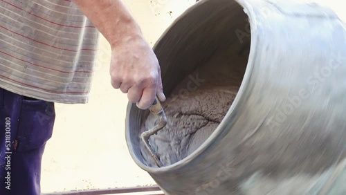 Man hand with a bricklayer spoon clean the mixer machine mouth in close up