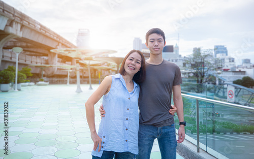 Mother and teenage son, tall, well-proportioned, good-looking, healthy, standing around the waist, embracing each other, smiling at the camera. There was an orange light shining from behind.