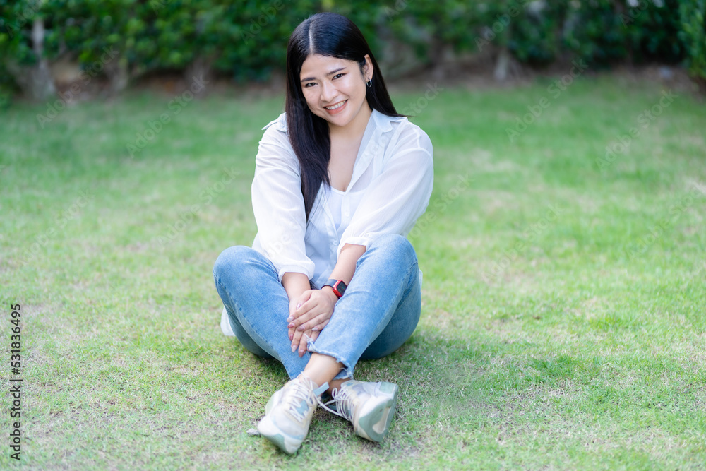 Modern portrait of beautiful happy Asian woman traveler wearing smartwatch wearing beautiful white dress and wear jeans lifestyle enjoying in sitting in the grass background Modern portrait of beautiful happy Asian woman traveler wearing smartwatch wearing beautiful white dress and wear jeans lifestyle enjoying in sitting in the grass background