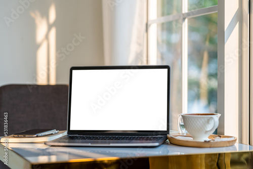 Mockup of laptop computer with empty screen with coffee cup and smartphone on table beside the window of the coffee shop background,White screen