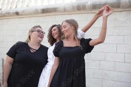 Tree friends, plus size woman and two strong girls walking in the streeet of the city against the urban whit wall. Female people dressed white and black dress photo