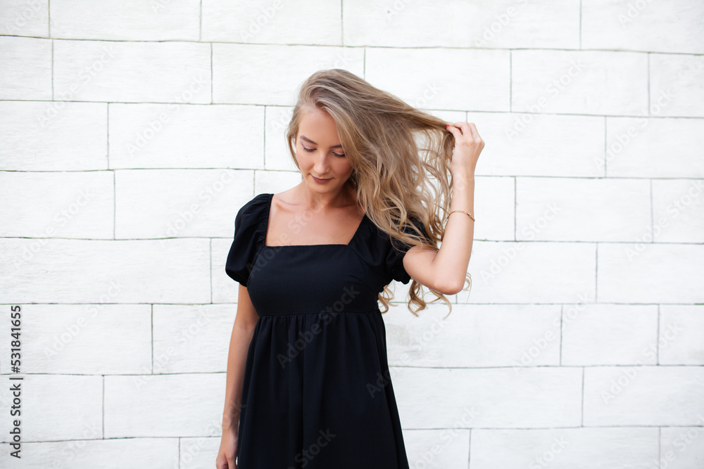 Beautiful natural blond woman with long hairs walking in the street . Girl dressed black dress and posing against street wall Beautiful natural blond woman with long hairs walking in the street . Girl dressed black dress and posing against street wall