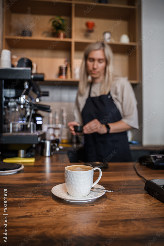 Shot of coffee cup on table and aged female barista with blond hairs. Shot of coffee cup on table and aged female barista with blond hairs.