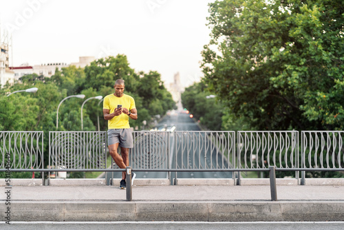 Sporty adult man using cellphone on sidewalk in the footbridge outdoors © santypan
