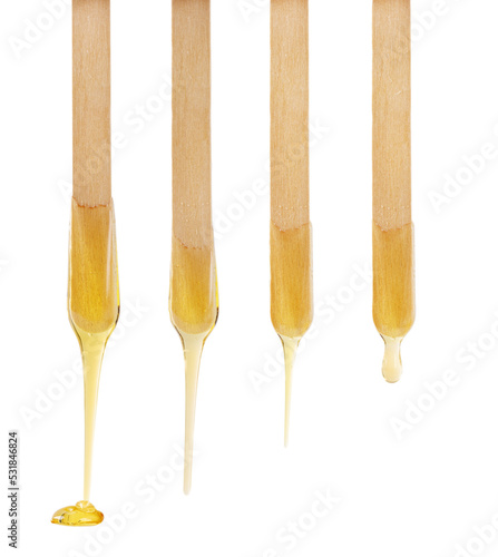 Golden sugar paste or wax for depilation dripping from wooden stick isolated on white background.