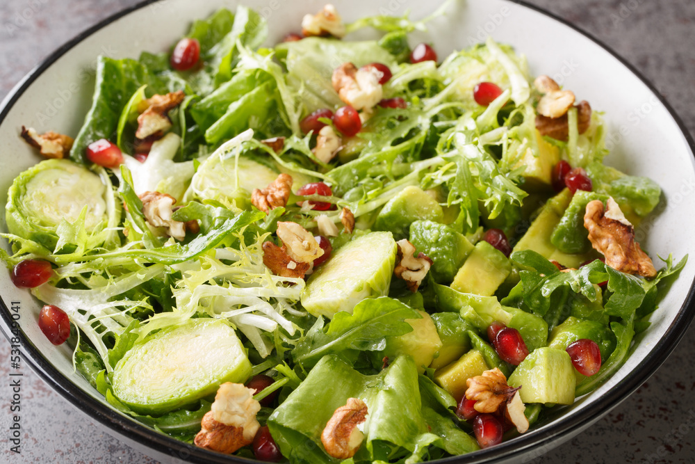 Raw Healthy salad with Brussels Sprouts Pomegranate, Avocado, walnuts and lettuce closeup in the bowl on the table. Horizontal Raw Healthy salad with Brussels Sprouts Pomegranate, Avocado, walnuts and lettuce closeup in the bowl on the table. Horizontal
