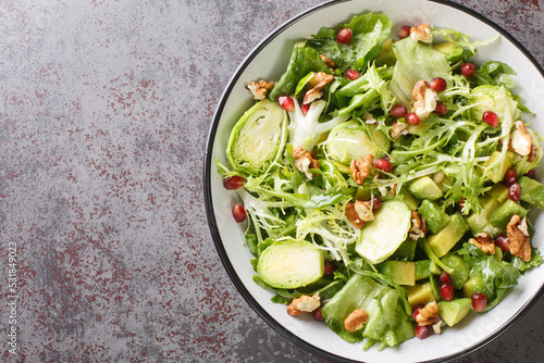 Raw Healthy salad with Brussels Sprouts Pomegranate, Avocado, walnuts and lettuce closeup in the bowl on the table. Horizontal top view from above