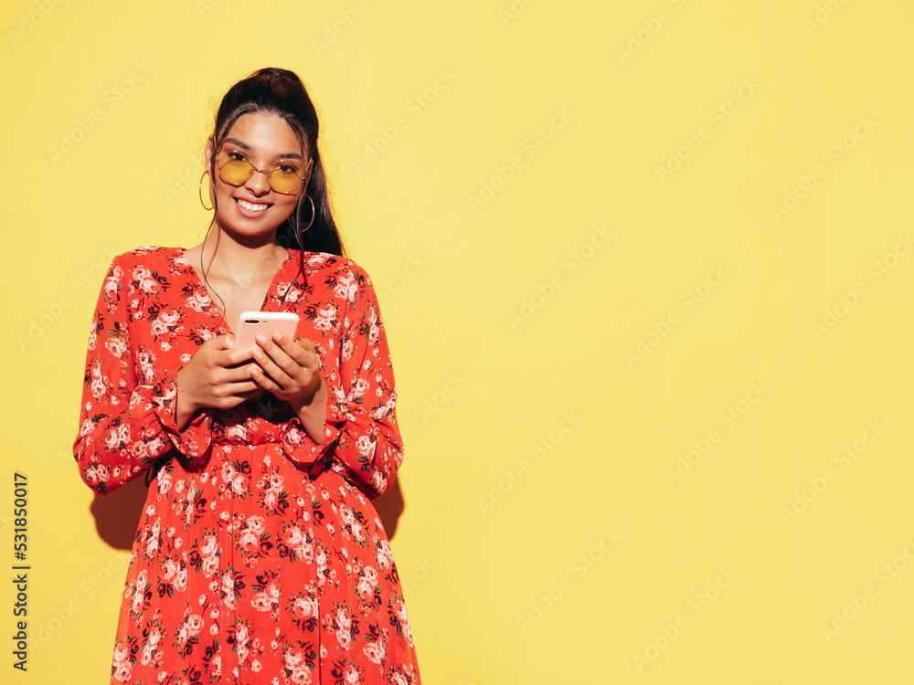 Young beautiful smiling female in trendy summer dress clothes. Sexy carefree woman posing near yellow wall in studio. Positive model having using phone apps. Holding smartphone, looking at screen Young beautiful smiling female in trendy summer dress clothes. Sexy carefree woman posing near yellow wall in studio. Positive model having using phone apps. Holding smartphone, looking at screen