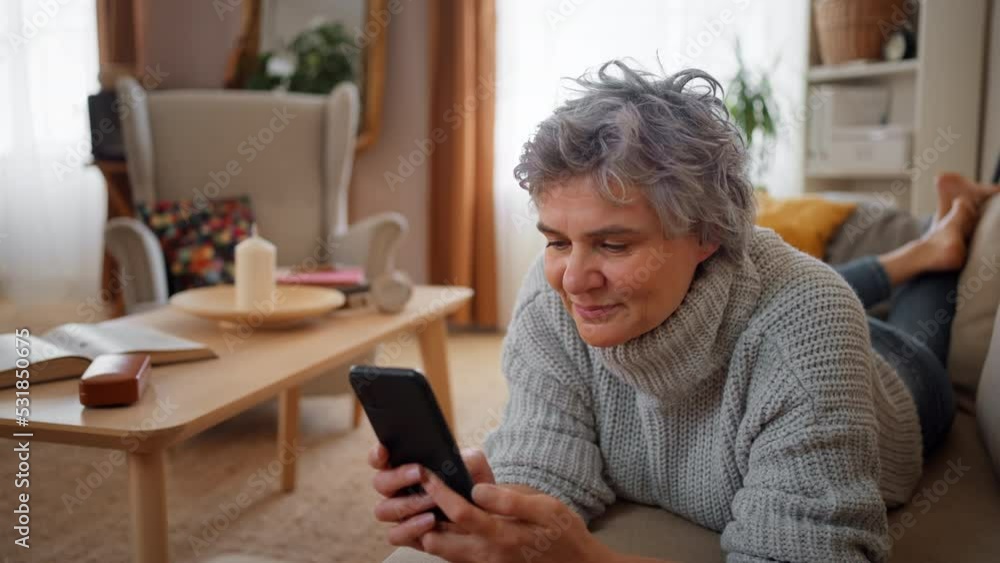 Smiling mature woman using smart phone while lying on sofa at home Smiling mature woman using smart phone while lying on sofa at home