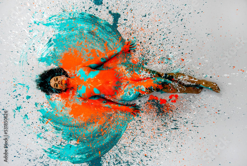 top view to sexy naked woman lying elegant on the floor in turquoise blue orange color abstractly painted bodypainting girl on splashed ground photo