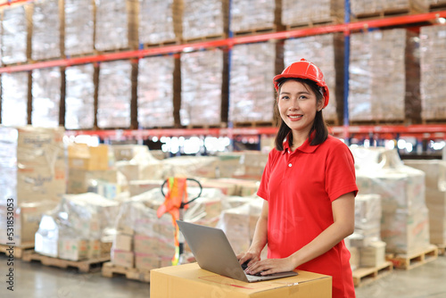 Portrait of warehouse workers young asian woman standing and using computer while looking at camera and controlling stock and inventory in retail warehouse logistics, distribution center