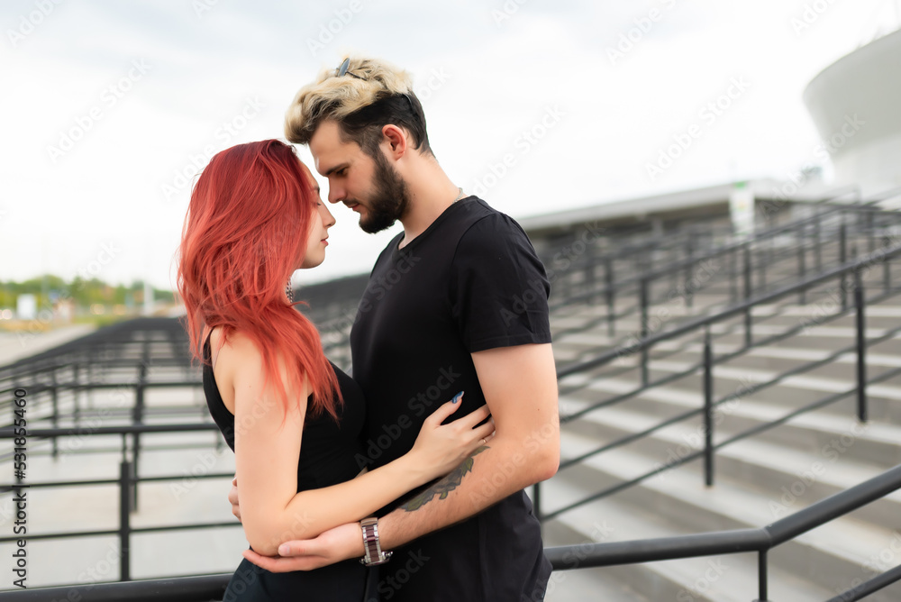 Stylish couple in love in black clothes walks in the park and hugs. Lovely couple of hipsters hugging on the background of the stairs. Youth, love and lifestyle concept