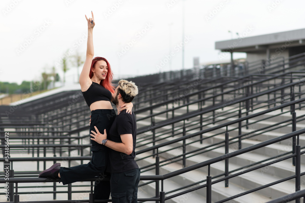 Stylish couple in love in black clothes walks in the park and hugs. Lovely couple of hipsters hugging on the background of the stairs. Emotional girl with hands up
