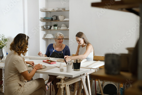 People working with clay in ceramic studio. Pottery workshop in studio. Adults learning to do ceramic plates. Pottery as hobby and leisure activity