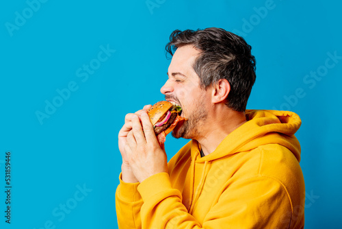  white guy in yellow hoodie eating hamburger on blue background