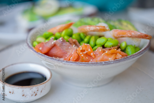 Side view on shrimp poke bowl with edamame beans, avocado, avocado and salmon.