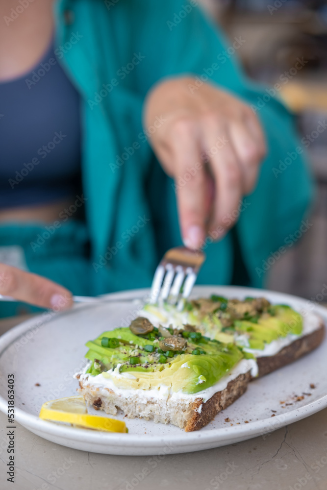 Woman eating avocado toast in cafe. Female hand cutting tasty sandwich or bruschetta.