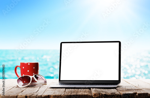 Laptop with blank screen and coffee cup in front of sunny sea