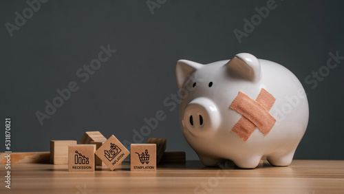 Broken piggy bank with bandages and wooden blocks with recession, inflation, stagflation icons. Basic financial concepts for a recession or bankruptcy. photo