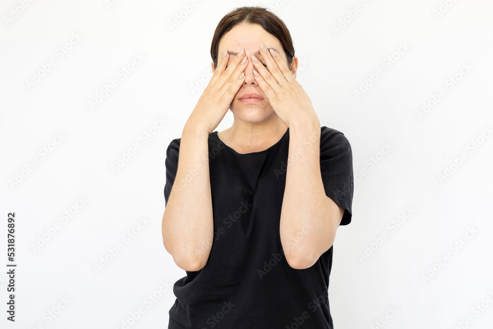 Portrait of young tired woman in black T-shirt covering eyes. Female model with plain face bored or unwilling to seeing anything. Portrait, studio shot, reluctance concept Portrait of young tired woman in black T-shirt covering eyes. Female model with plain face bored or unwilling to seeing anything. Portrait, studio shot, reluctance concept