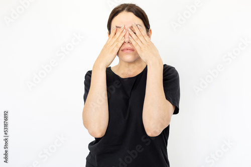 Portrait of young tired woman in black T-shirt covering eyes. Female model with plain face bored or unwilling to seeing anything. Portrait, studio shot, reluctance concept