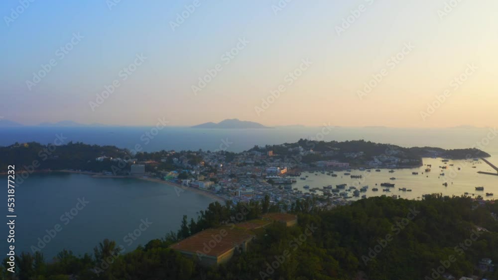 Drone shot traveling upward above an island during golden hour toward a little city built on an isthmus with a beach and an harbor . Drone shot traveling upward above an island during golden hour toward a little city built on an isthmus with a beach and an harbor .