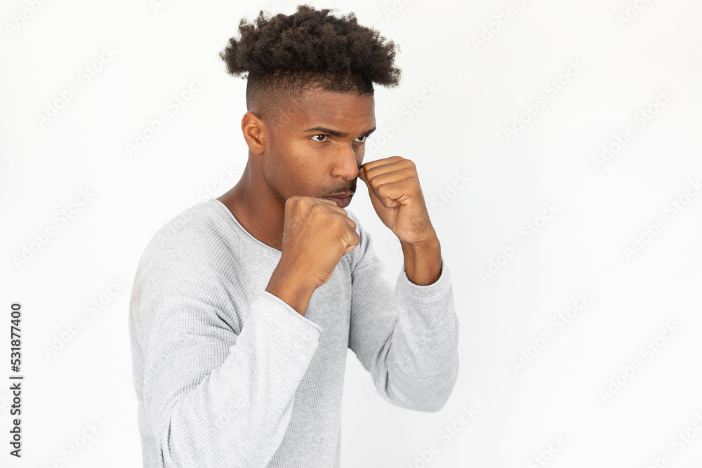 Confident African American man standing in boxing stance. Portrait of young bearded guy wearing white sweater clenching fists and looking away against white background. Conflict and defense concept Confident African American man standing in boxing stance. Portrait of young bearded guy wearing white sweater clenching fists and looking away against white background. Conflict and defense concept