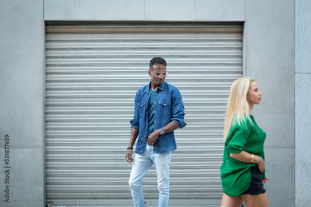 African man looking at a blonde woman as she pass in the street