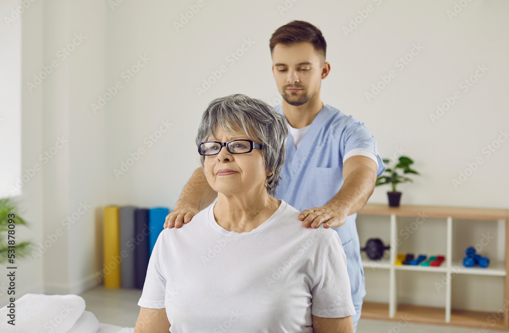 Male physiotherapist help elderly female patient with back pain or trauma. Therapist or masseur work exercise with mature woman client in clinic for soon recovery. Rehabilitation concept. Male physiotherapist help elderly female patient with back pain or trauma. Therapist or masseur work exercise with mature woman client in clinic for soon recovery. Rehabilitation concept.