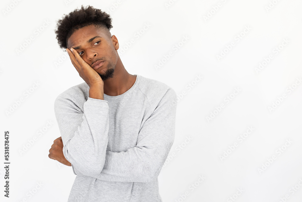 Portrait of bored African American man looking away. Young bearded guy wearing white sweater standing leaning on hand against white background. Boredom and depression concept Portrait of bored African American man looking away. Young bearded guy wearing white sweater standing leaning on hand against white background. Boredom and depression concept