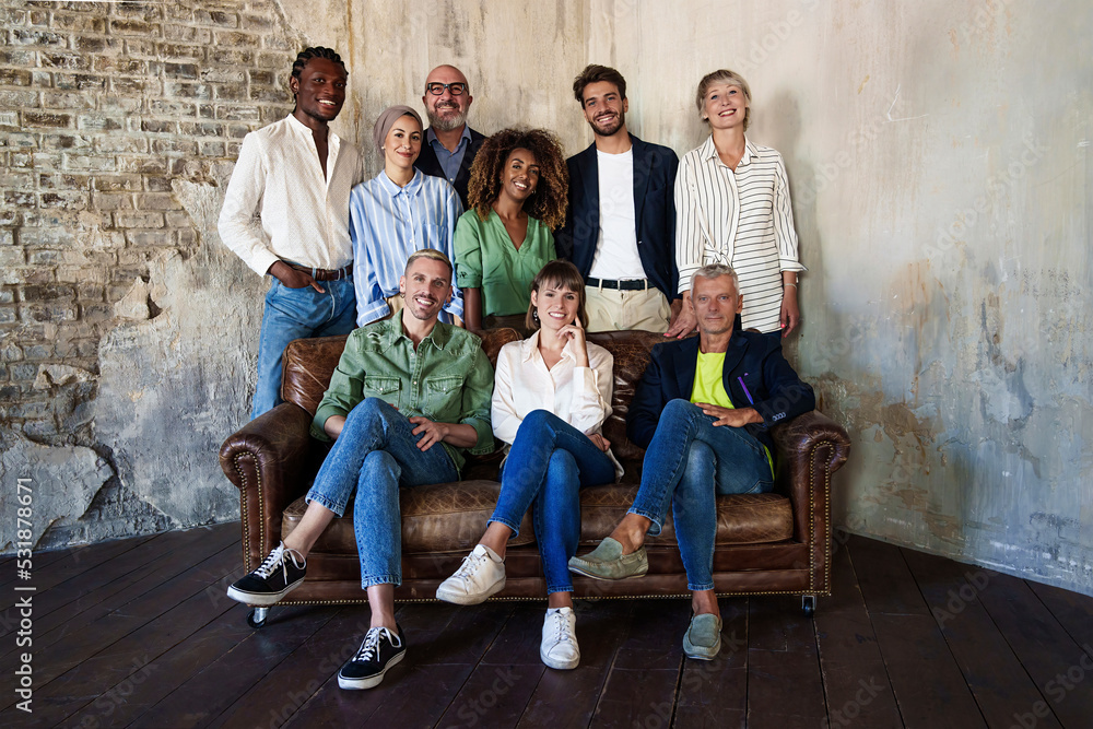 Portrait of arranged multiracial colleagues sitting on a sofa and standing together against a concrete wall