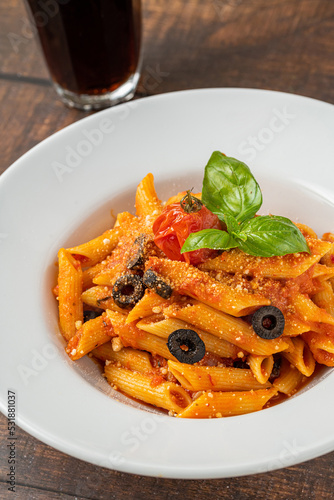 Penne pasta in tomato sauce  tomatoes decorated with parsley on a wooden background