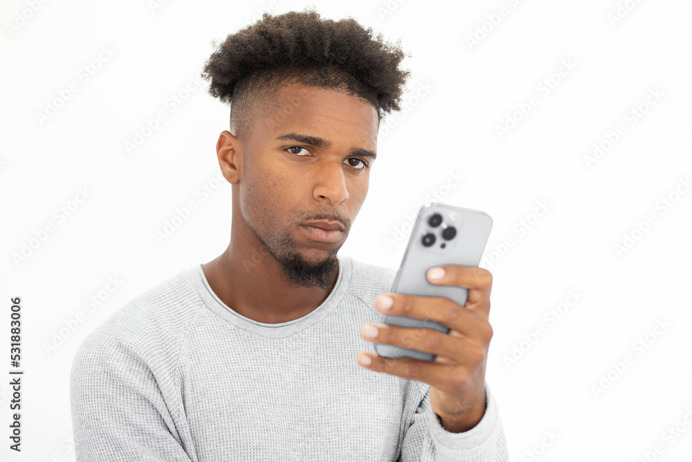 Portrait of skeptic African American man holding mobile phone. Young bearded guy wearing white sweater using smarpthone and looking at camera against white background. Mobile technology concept Portrait of skeptic African American man holding mobile phone. Young bearded guy wearing white sweater using smarpthone and looking at camera against white background. Mobile technology concept