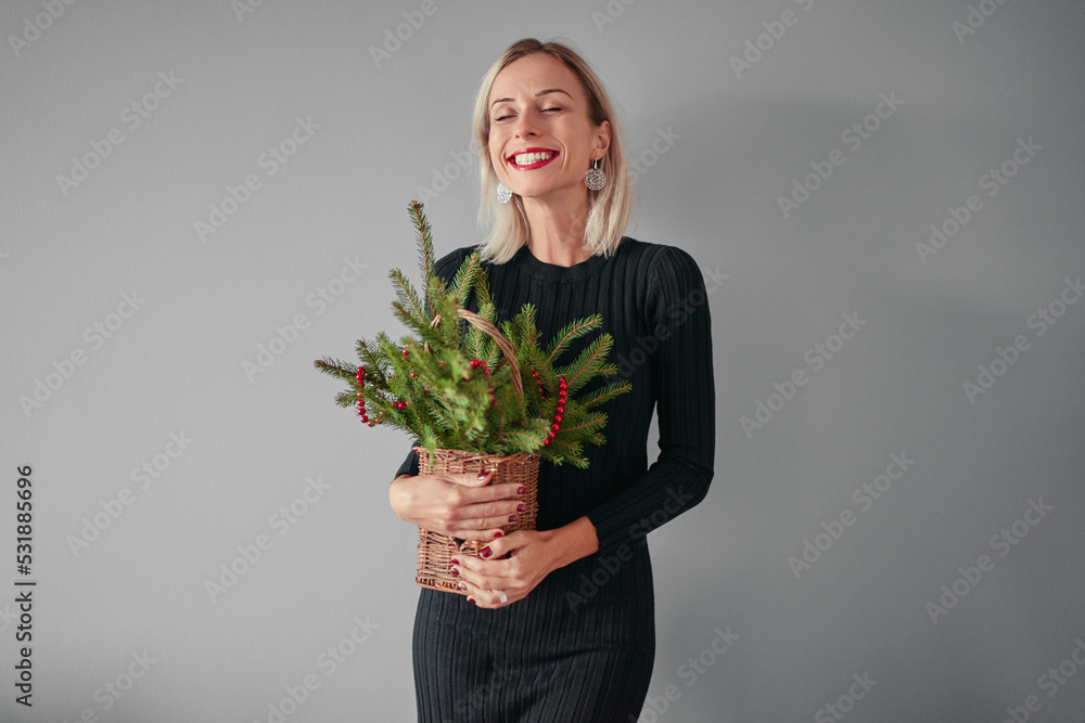 Happy young woman holding bouquet of pine tree branch against grey background. Happy young woman holding bouquet of pine tree branch against grey background.