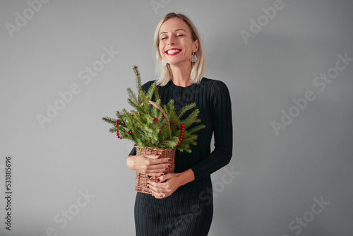 Happy young woman holding bouquet of pine tree branch against grey background.