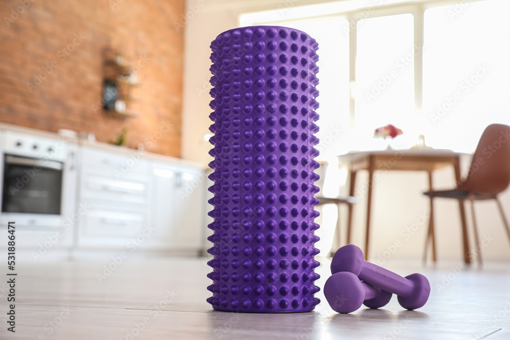 Naklejka premium Foam roller with dumbbells on floor in kitchen