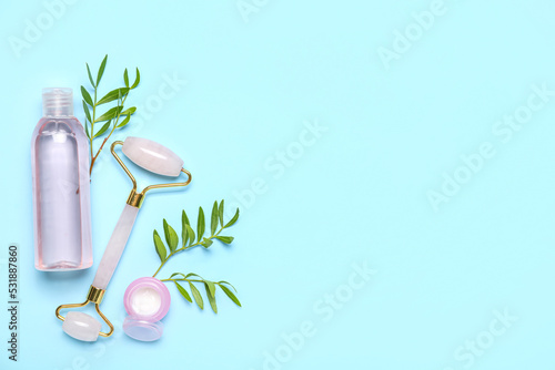 Fototapeta Naklejka Na Ścianę i Meble -  Facial massage tool with cosmetic bottle, jar of cream and plant branches on blue background