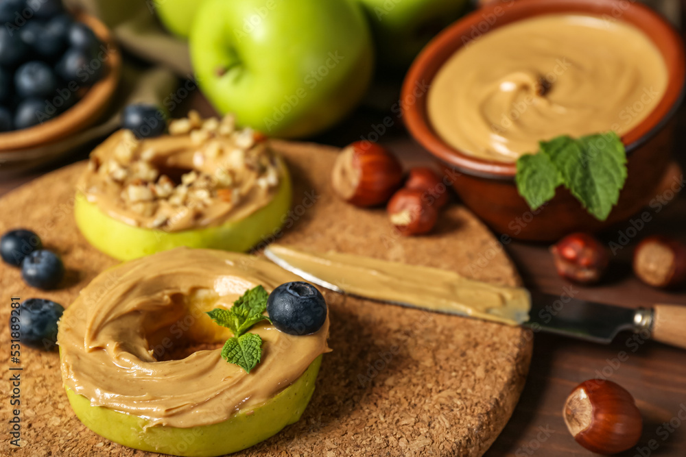 Cork mat of tasty apple rounds with nut butter on wooden table, closeup Cork mat of tasty apple rounds with nut butter on wooden table, closeup