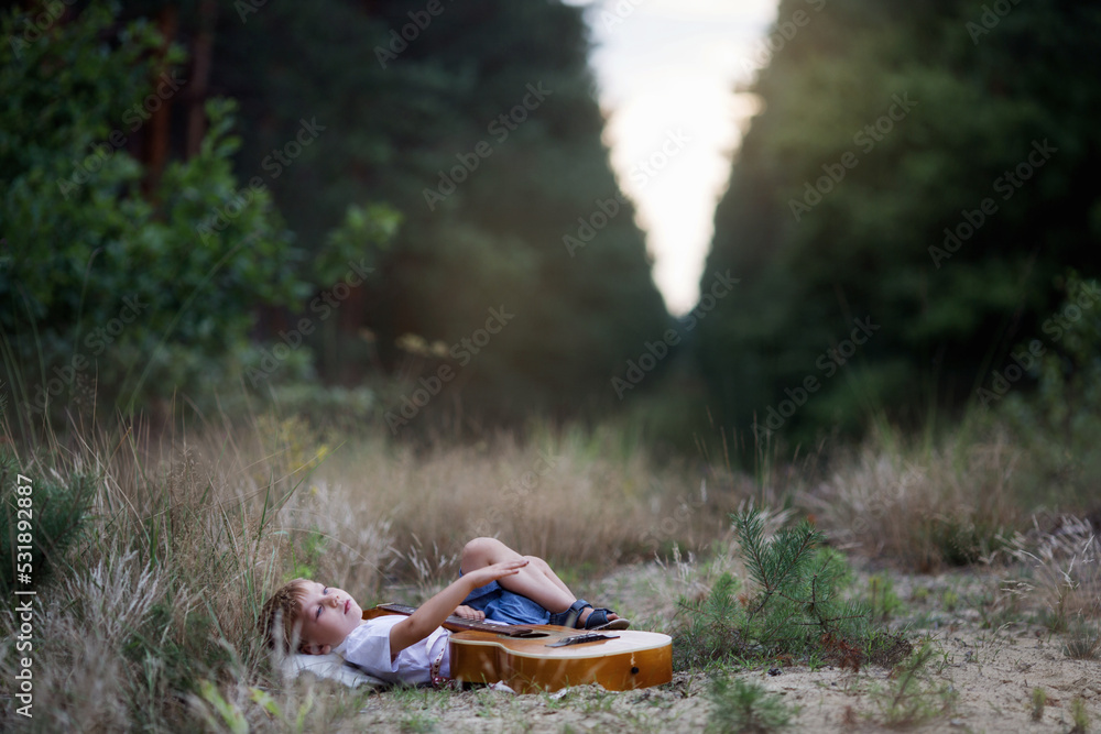 Chłopiec leży na trawie i gra na gitarze - obrazy, fototapety, plakaty 