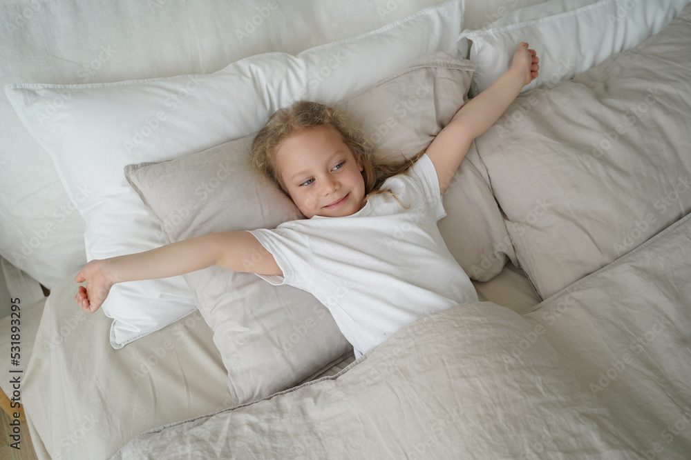 Happy little child girl stretching, lying in soft bed after wake up. Healthy children's sleep Happy little child girl stretching, lying in soft bed after wake up. Healthy children's sleep