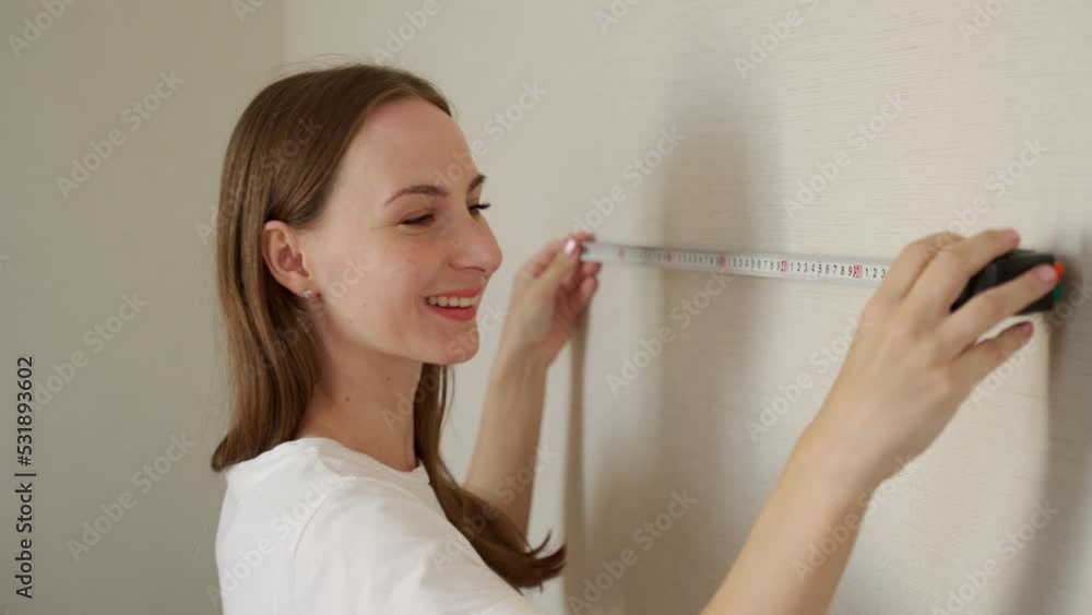 A woman with a meter in her hands, measuring the dimensions of the wall - the concept of home improvement with her own hands. A woman with a meter in her hands, measuring the dimensions of the wall - the concept of home improvement with her own hands.
