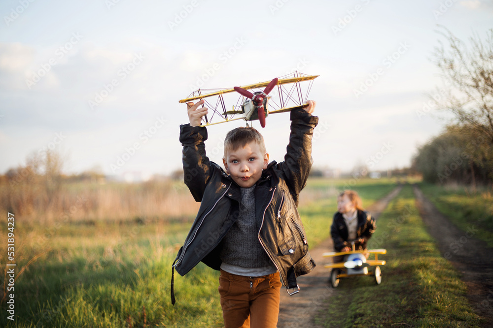 Chłopcy spełniają marzenie o lataniu, biegną drogą z samolotem w ręce - obrazy, fototapety, plakaty 