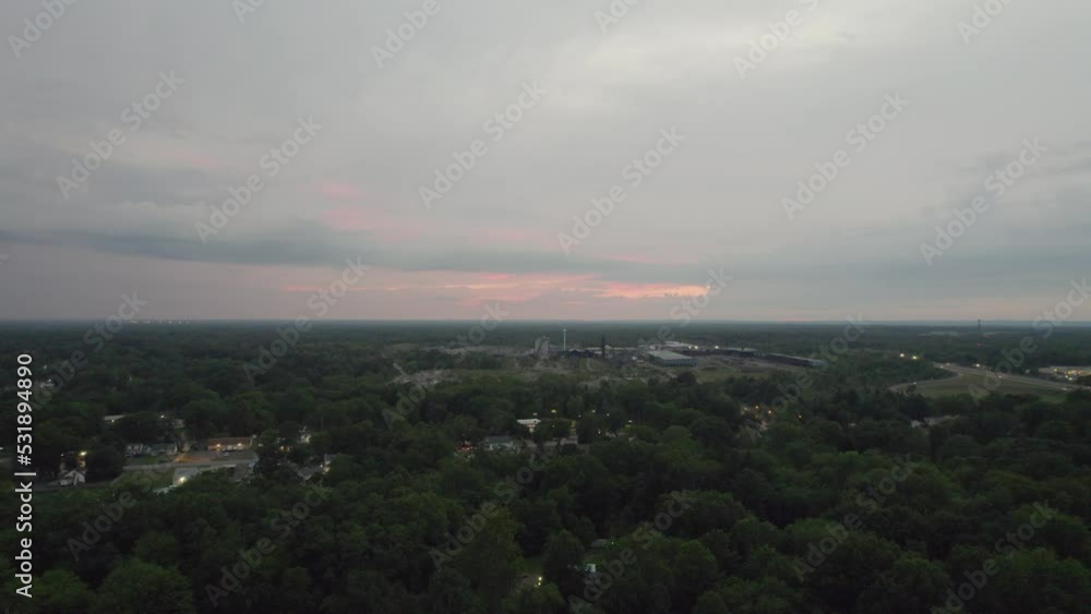 Aerial drone forward moving shot over an old mill alongside a small town surrounded by dense vegetation on a cloudy sunset. Aerial drone forward moving shot over an old mill alongside a small town surrounded by dense vegetation on a cloudy sunset.